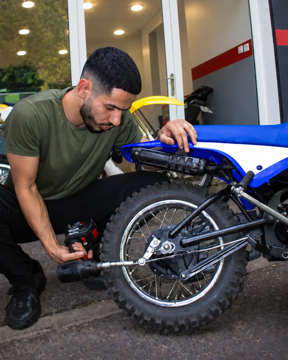 Un mécanicien utilise un outil sur la roue arrière d’une moto Off-road.